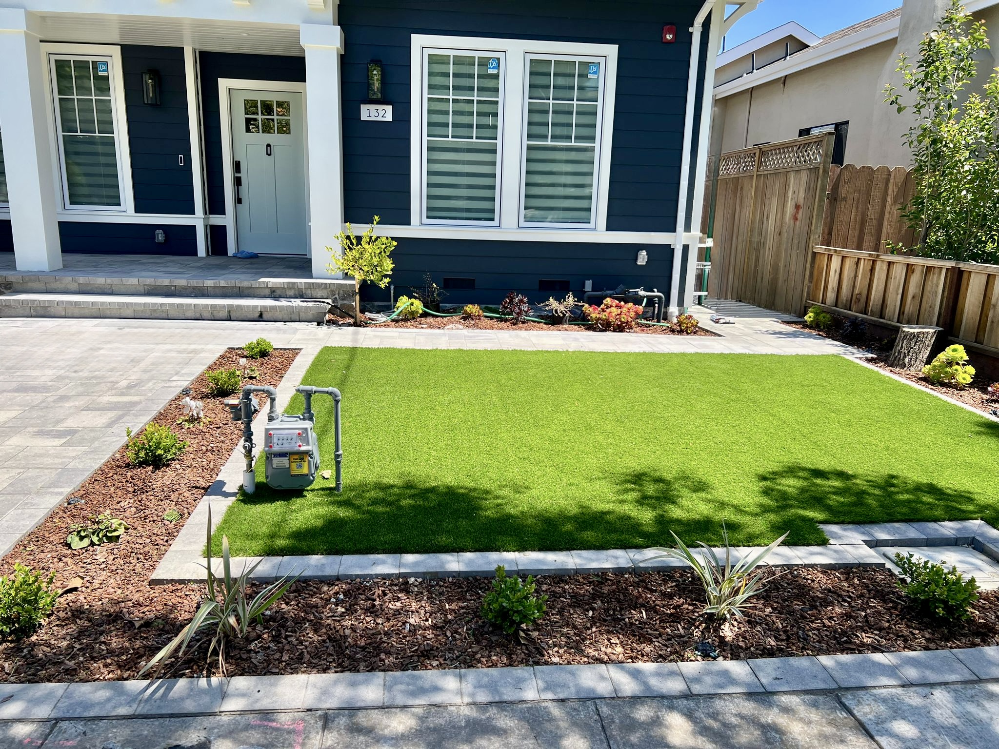 Front yard with artificial turf lawn, paver borders, and young plantings