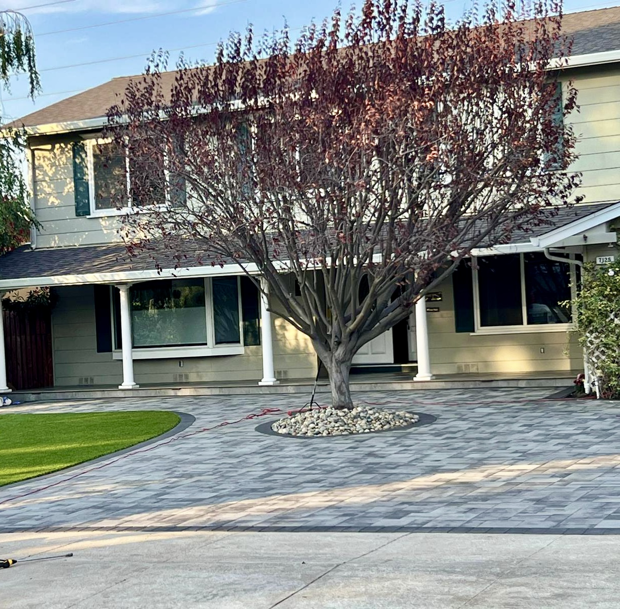 Beautiful front yard with paver driveway, artificial turf, and decorative tree