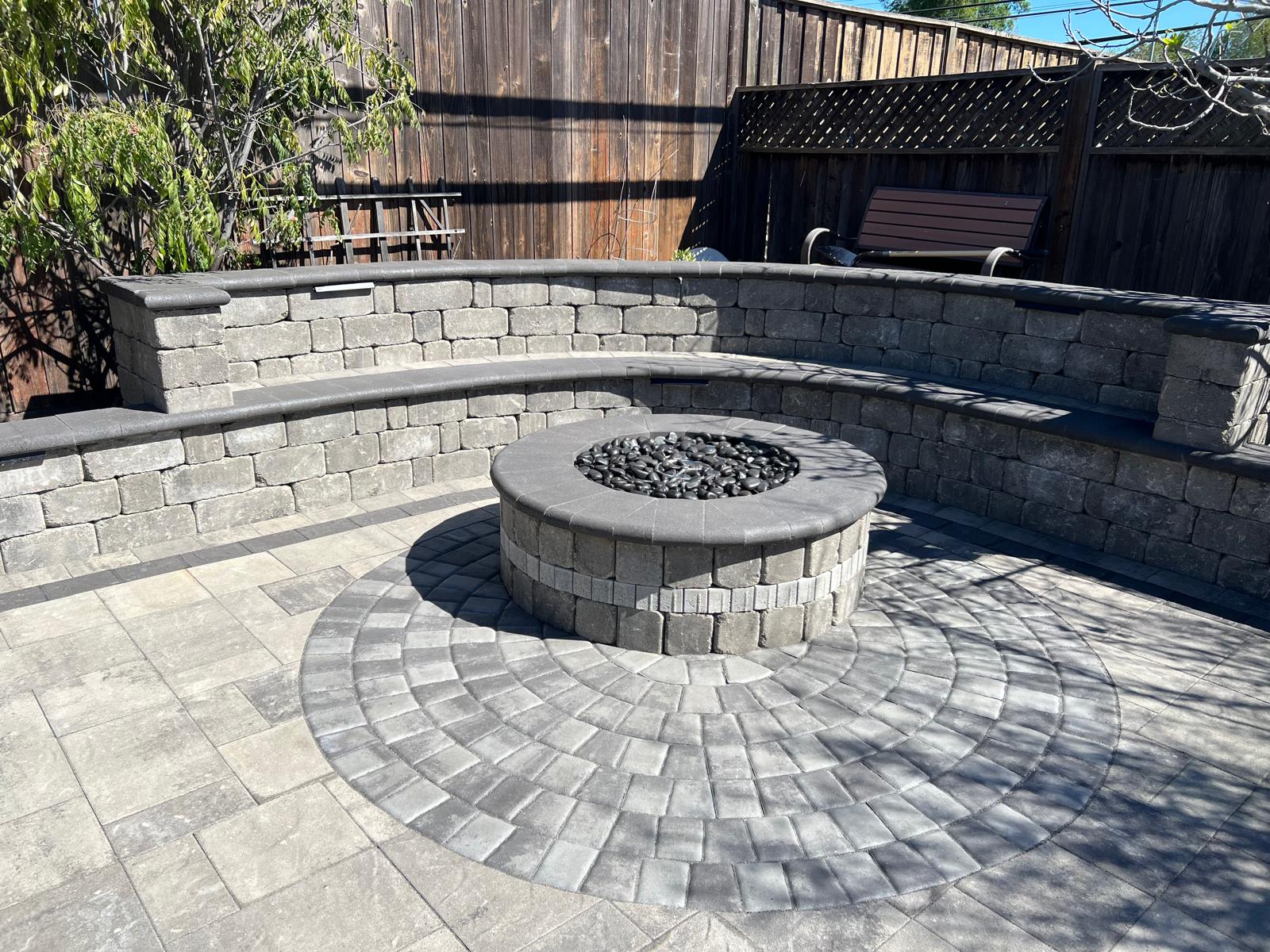 Close-up view of circular stone firepit with radiating paver pattern and stone seating walls