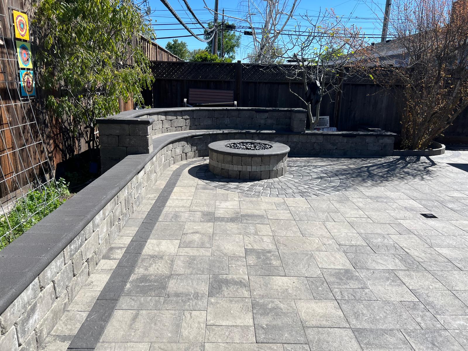 Another angle of stone patio showing curved retaining wall and firepit