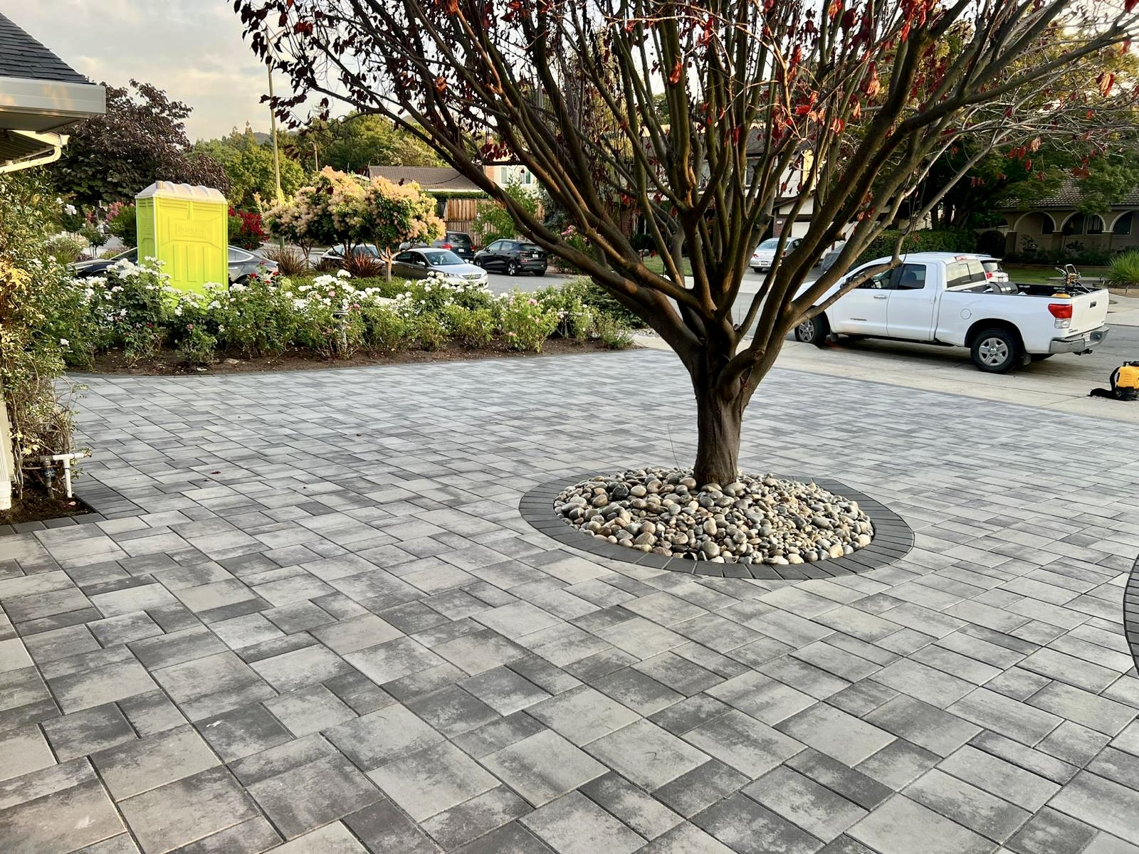 Paver driveway with decorative tree well and river rocks